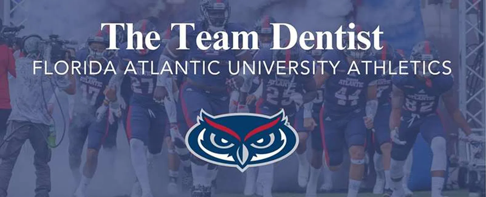 Florida Atlantic University football players run onto the field with team dentist sponsorship banner and owl logo.