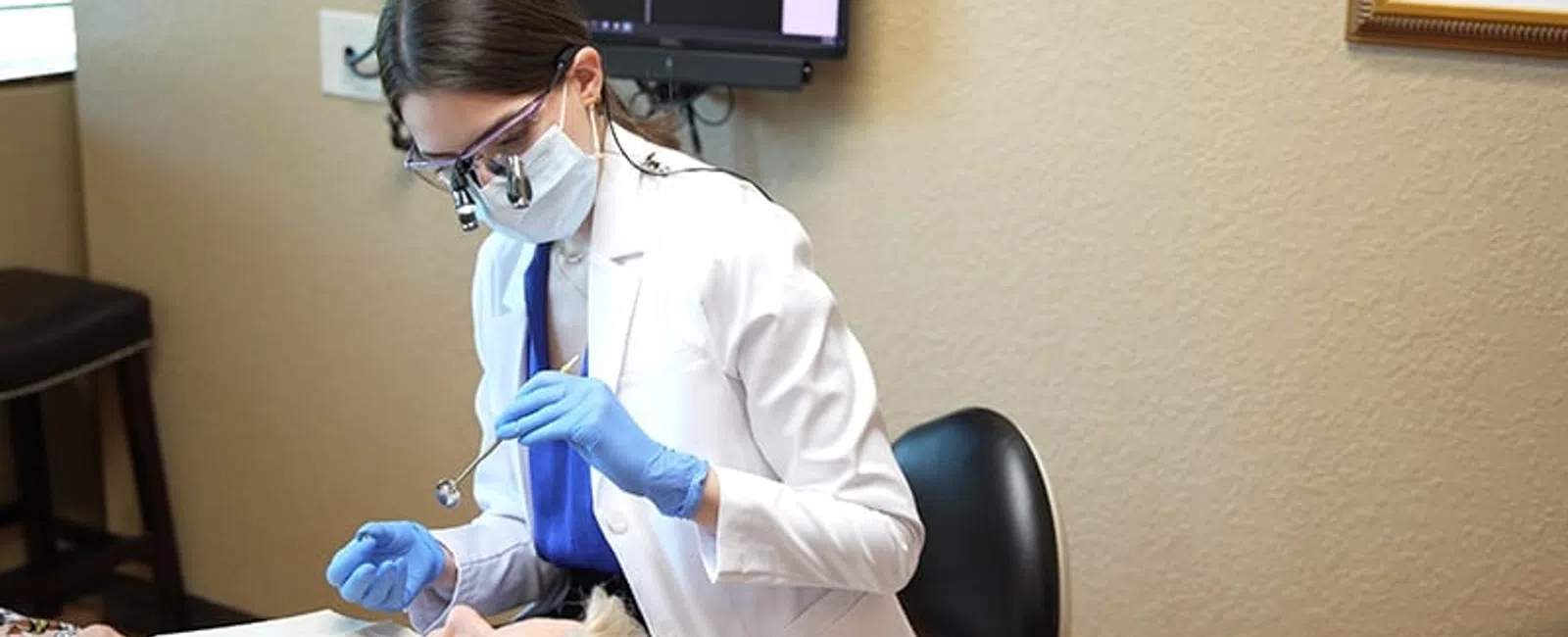 Dentist wearing protective gear examining elderly patient's teeth in a modern dental clinic setting.