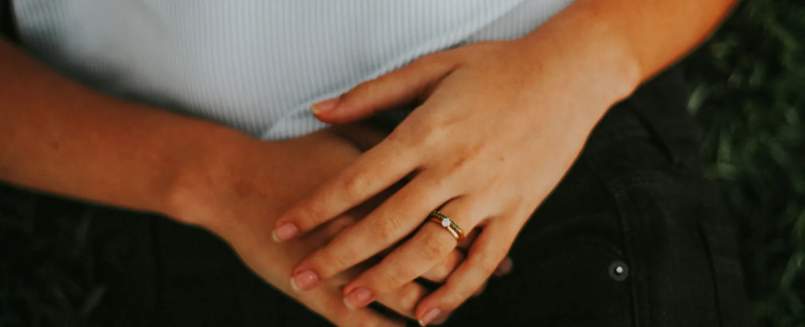 Close-up of hands resting on lap with a gold ring featuring a small gemstone on finger.