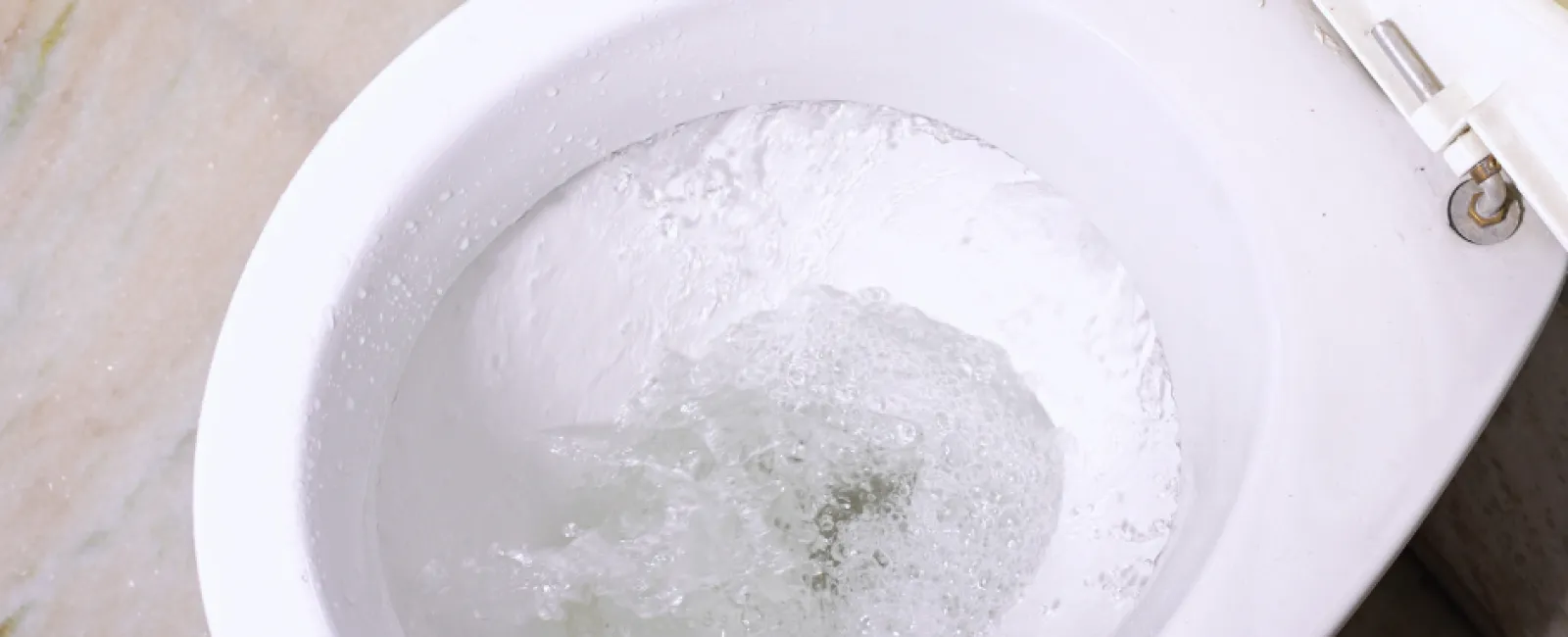 Top view of a white toilet bowl flushing with water swirling inside on marble floor.