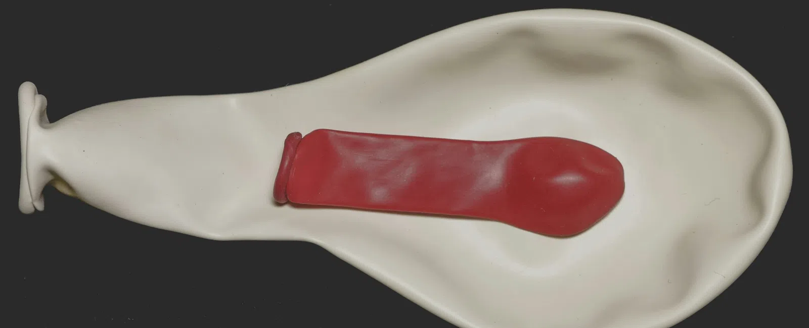 Deflated white balloon with a smaller deflated red balloon inside against a black background