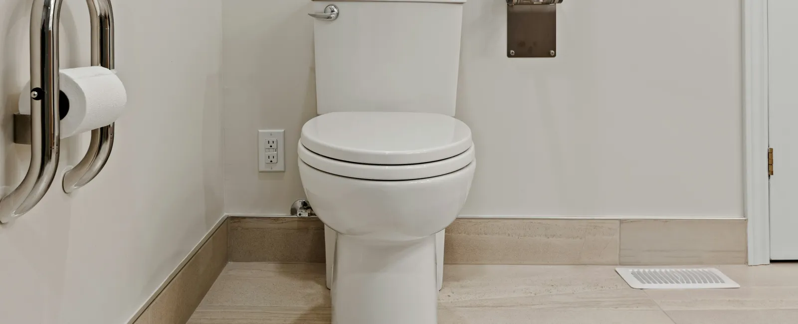 White toilet in a clean bathroom with beige tile floor and stainless steel grab bars for accessibility.