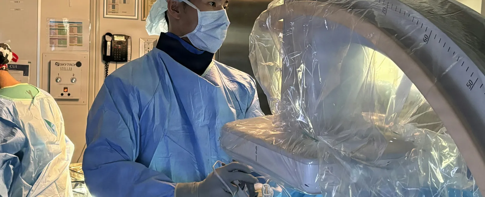 Surgeon in protective gear operating advanced medical imaging equipment in a hospital surgical room.