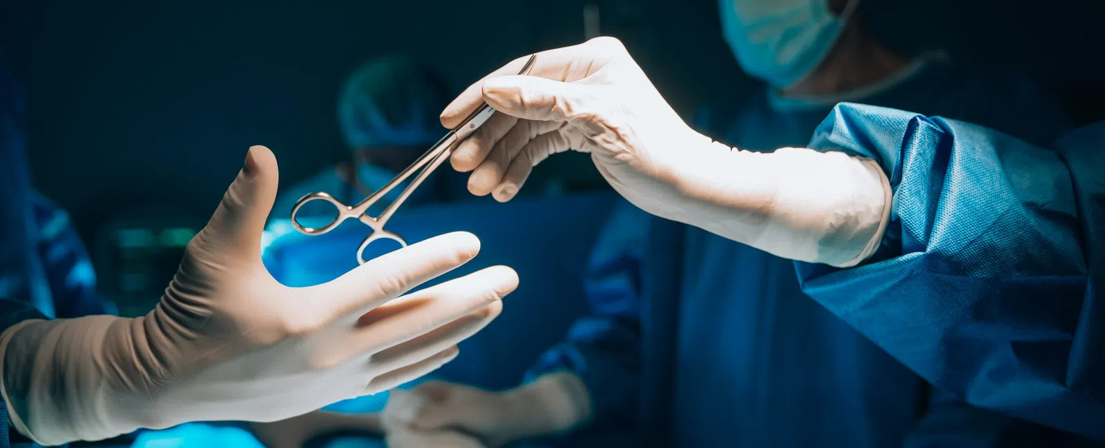 Surgeons in sterile gloves passing surgical scissors during an operation in a bright operating room.