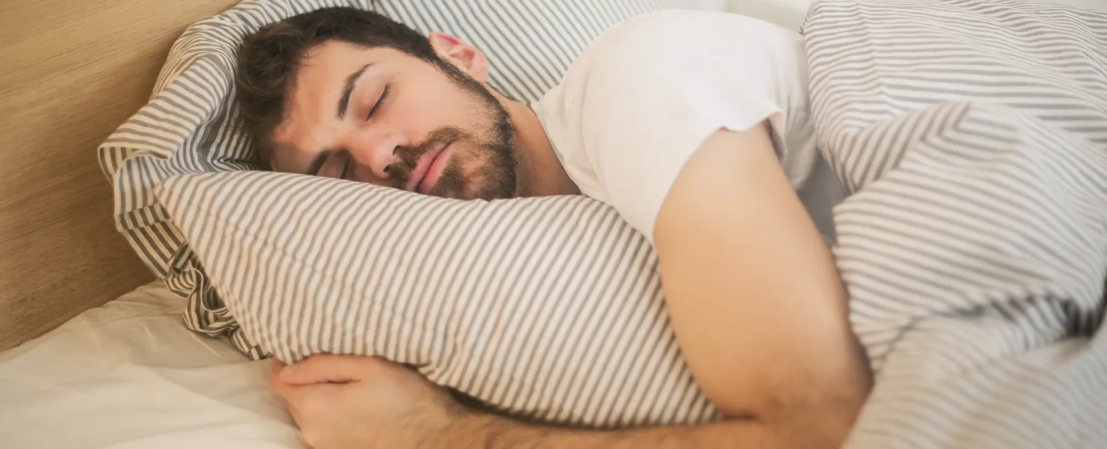 Man peacefully sleeping on bed hugging striped pillow with matching striped duvet in bright room