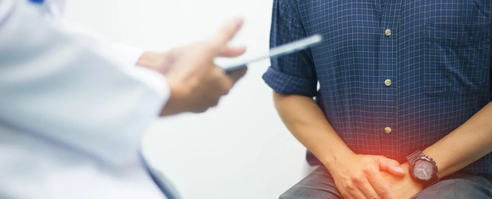 Man in blue shirt with hands on lower abdomen showing pain during a medical consultation with doctor.