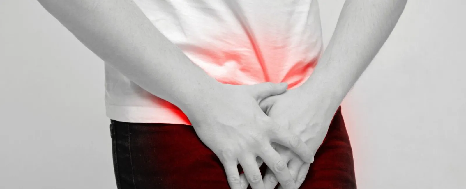 Person clutching lower abdomen and groin area showing pain or discomfort highlighted in red.