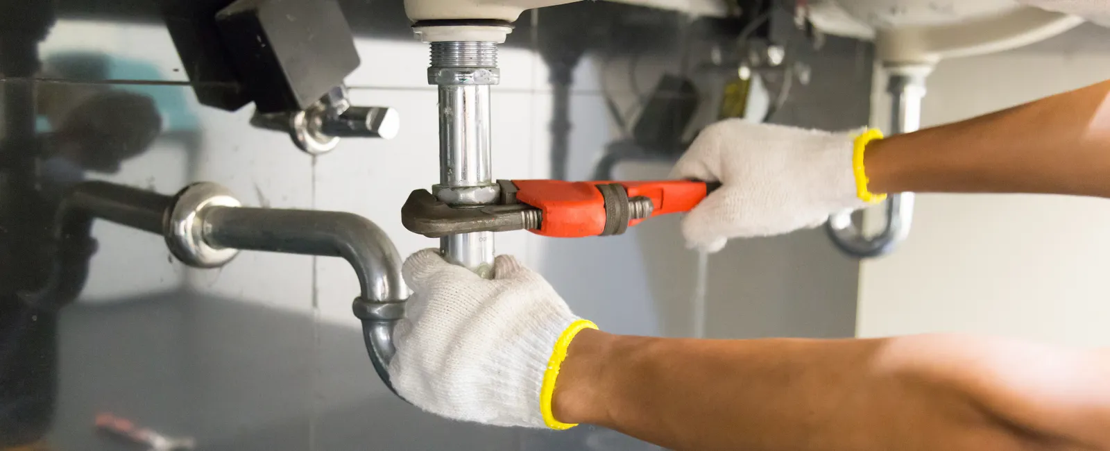 Plumber wearing gloves using a wrench to tighten pipes under a sink in a bathroom or kitchen