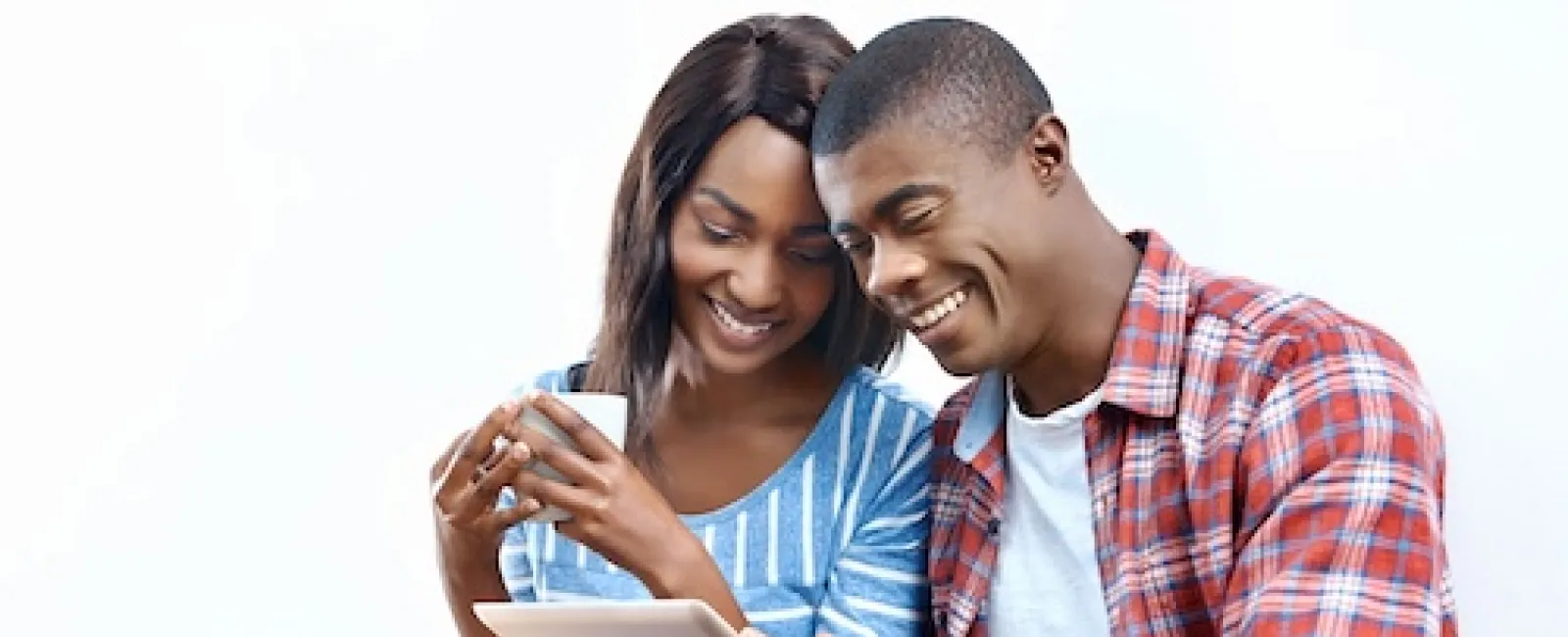 Happy couple sitting on floor, smiling and using tablet together, woman holding coffee cup relaxed at home.