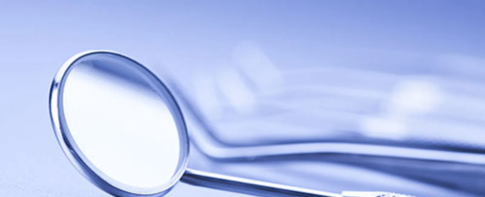 Close-up of a dental mirror with textured handle on a smooth surface with a blue tint background.