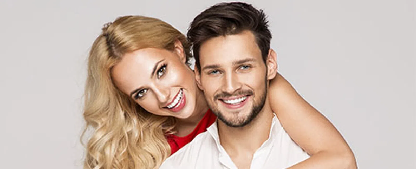 Happy young couple smiling, embracing each other against a neutral background, showing affection and joy.