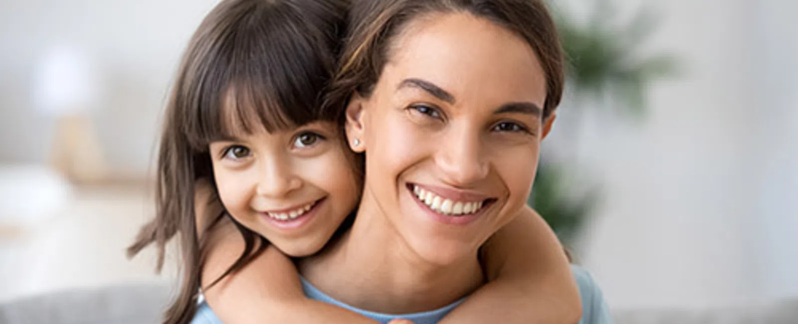 Smiling young woman with her arms around a happy girl, both close and joyful indoors.
