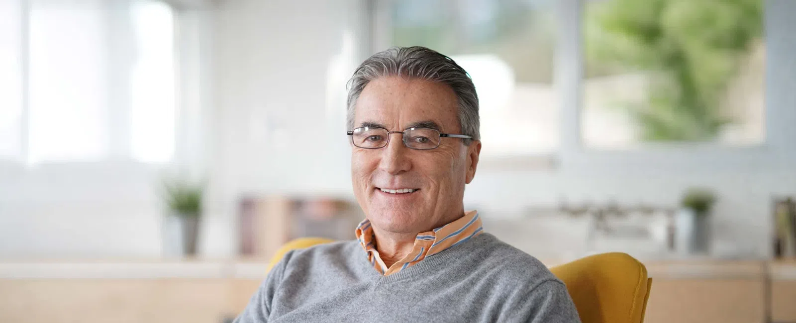 Smiling middle-aged man wearing glasses and grey sweater sitting comfortably in a bright modern office.