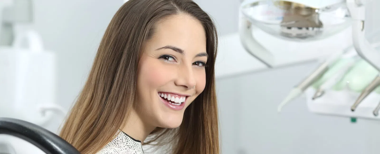 Smiling young woman sitting in a modern dental clinic chair with dental tools in the background