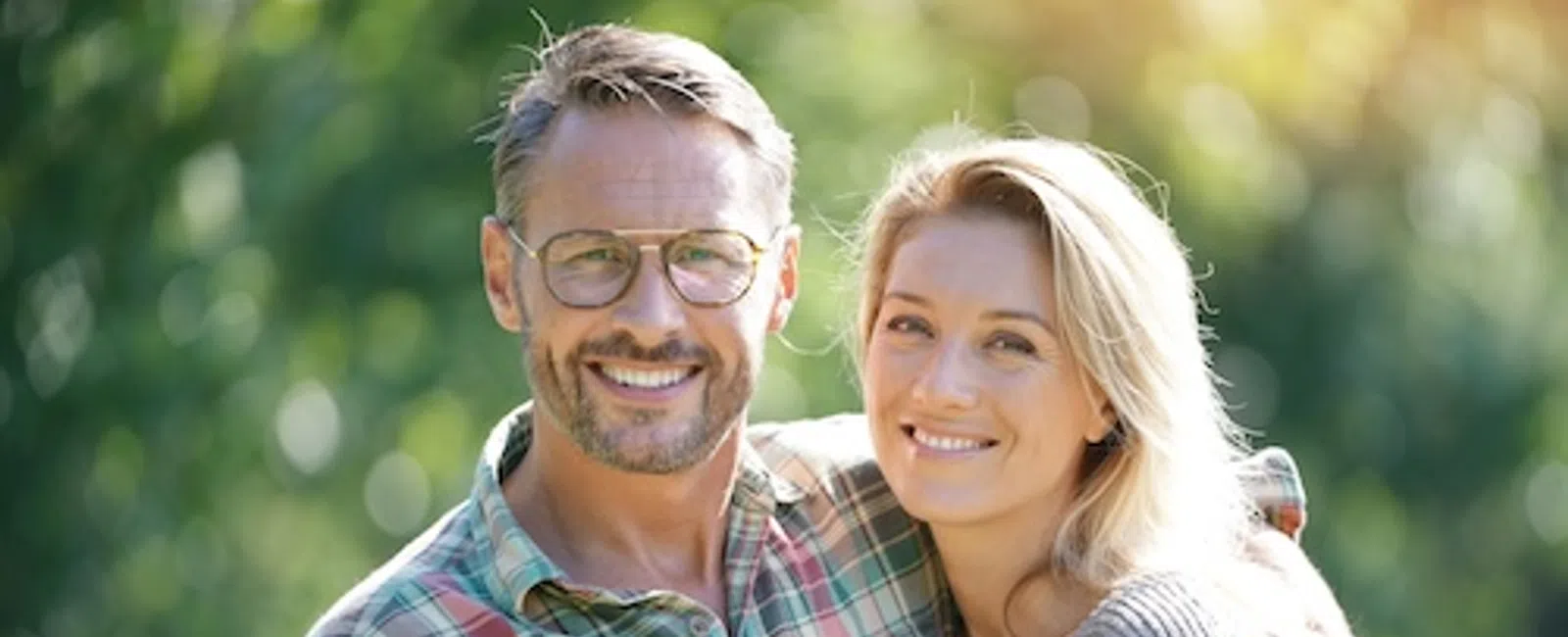 Smiling mature couple embracing outdoors with blurred green background on a sunny day