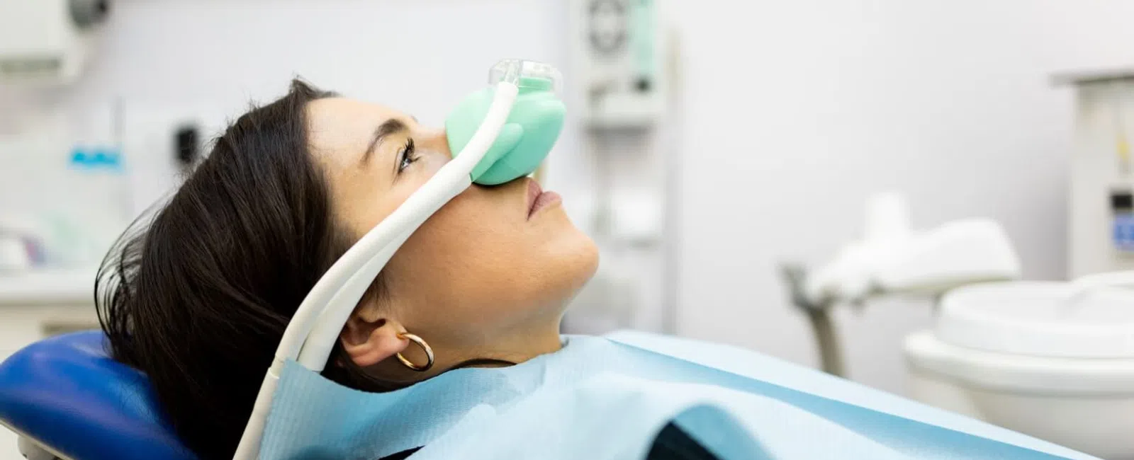 Woman reclining in dental chair wearing nitrous oxide mask and dental bib during treatment.