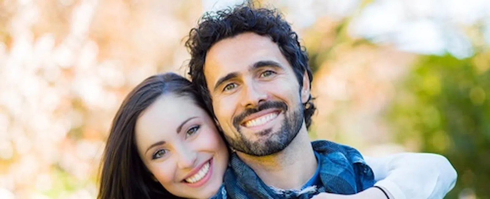 Happy young couple smiling and embracing outdoors with a blurred natural background in daylight.