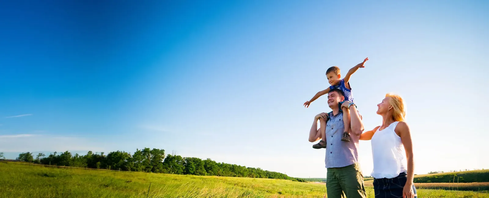 Happy family enjoying a sunny day outdoors in a green field with a clear blue sky.
