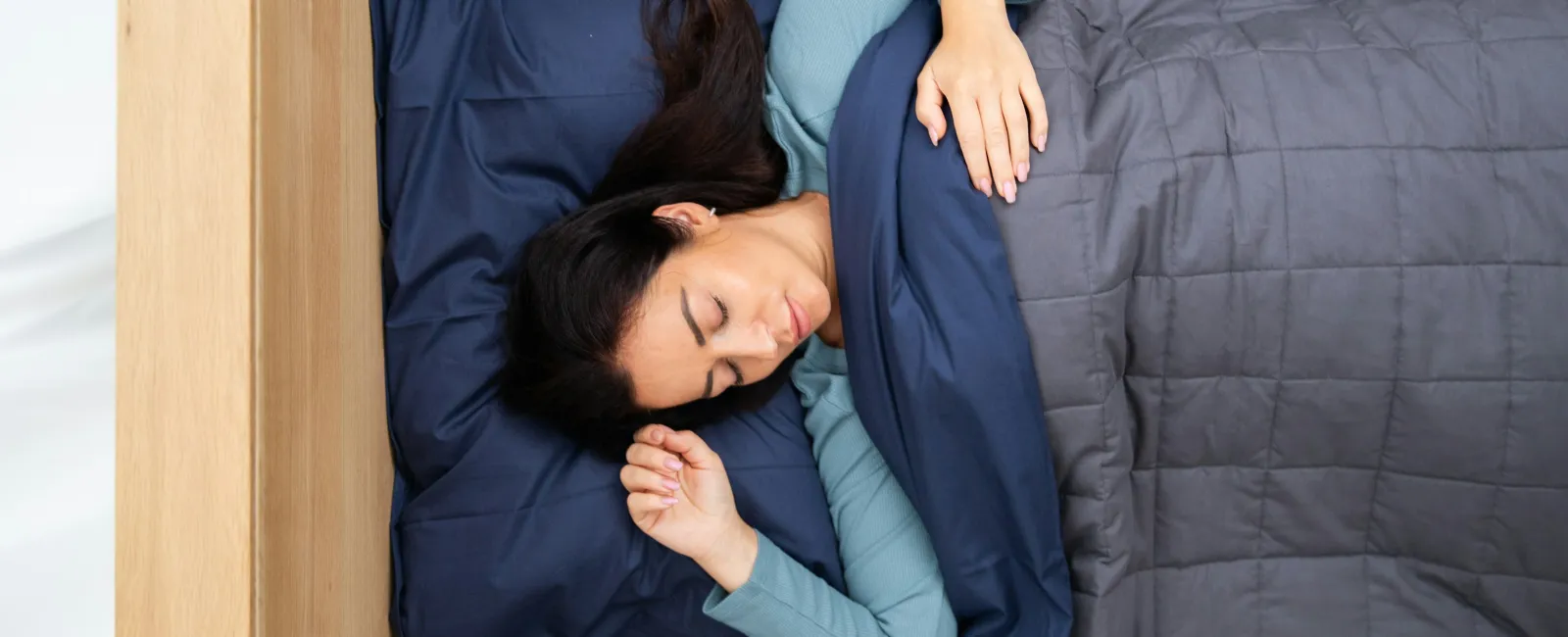 Woman sleeping peacefully in bed under a gray quilt and blue pillow, wearing a light blue long-sleeve shirt.