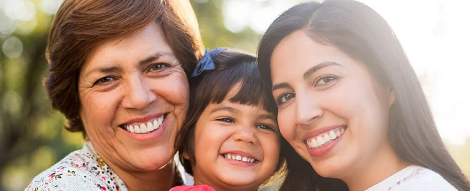 A joyful three-generation family portrait in a sunlit park, showcasing happiness and love.