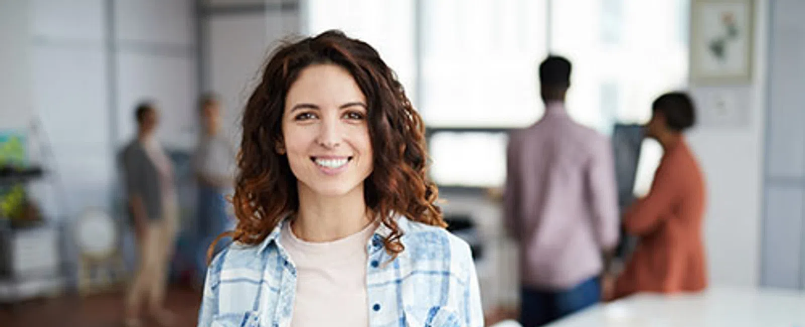 Smiling woman holding tablet in modern office with colleagues working in background