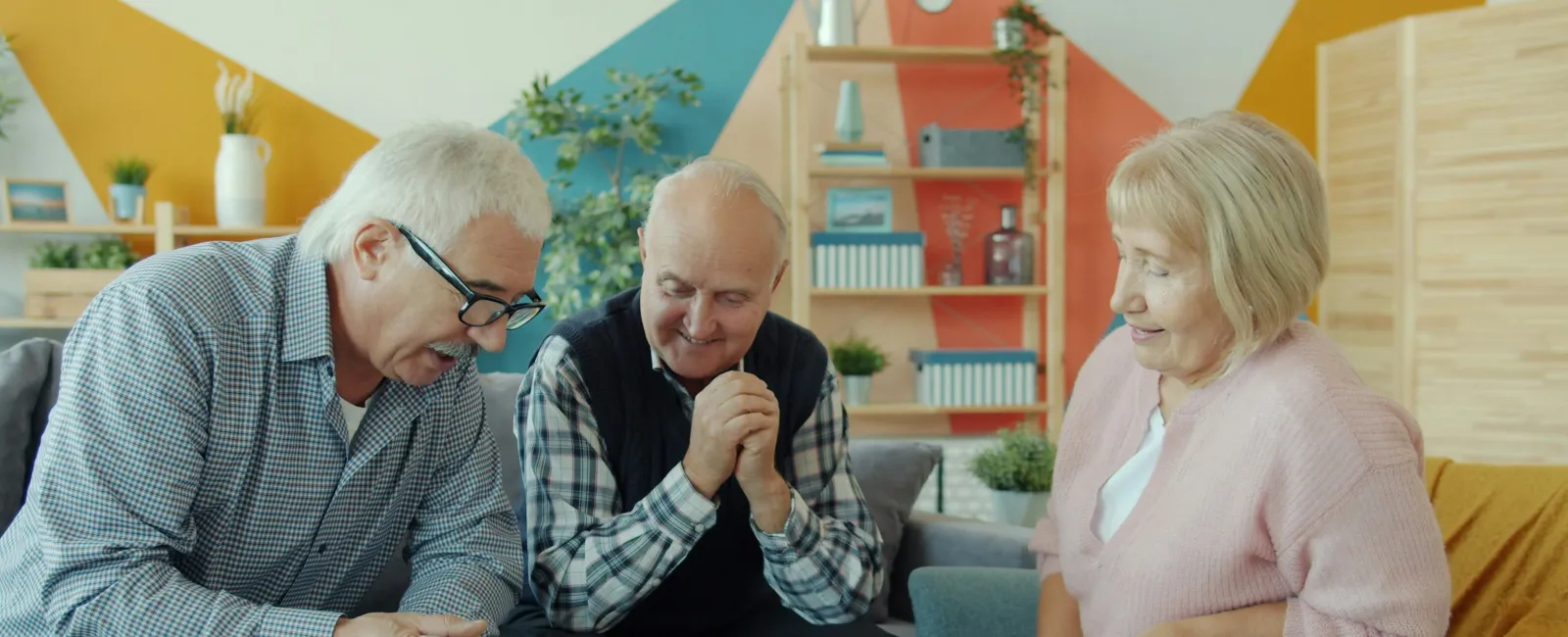 Three seniors playing chess together in a cozy room with colorful walls and tea cups on the table
