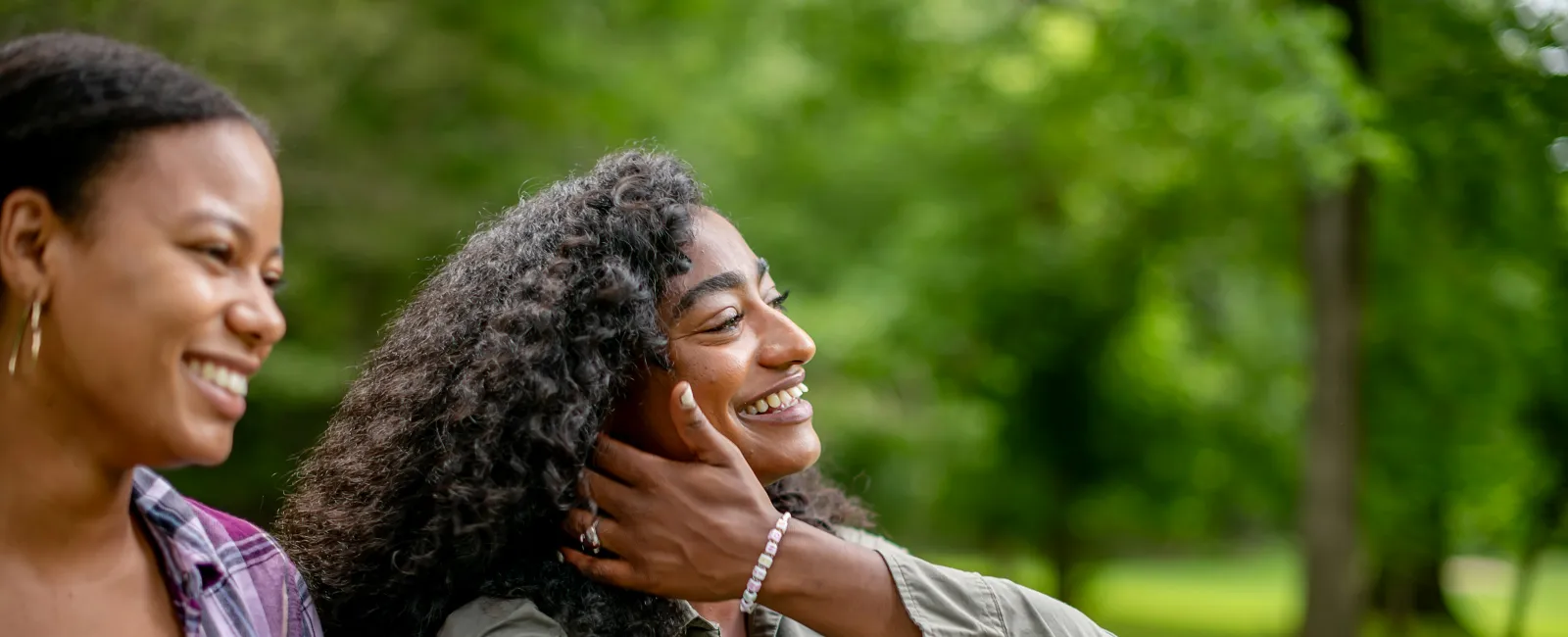 Two young women smiling and enjoying a sunny day sitting on grass in a green park outdoors.