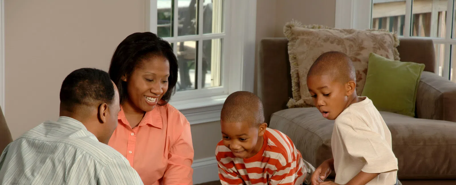 Family of four enjoying a board game together in a cozy living room with natural light.