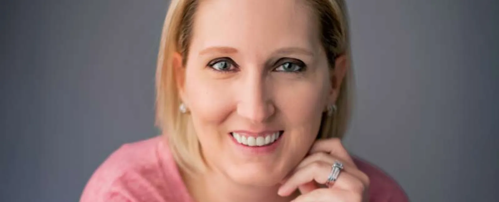 Smiling woman with blonde hair wearing a pink shirt showing white teeth after dental veneers and crowns.