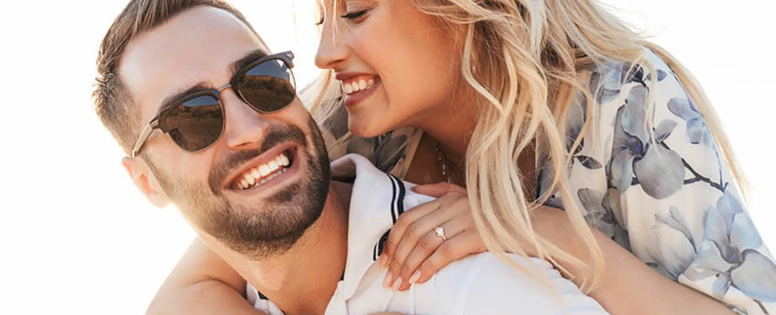 Happy couple enjoying a sunny day at the beach, smiling and embracing each other closely.