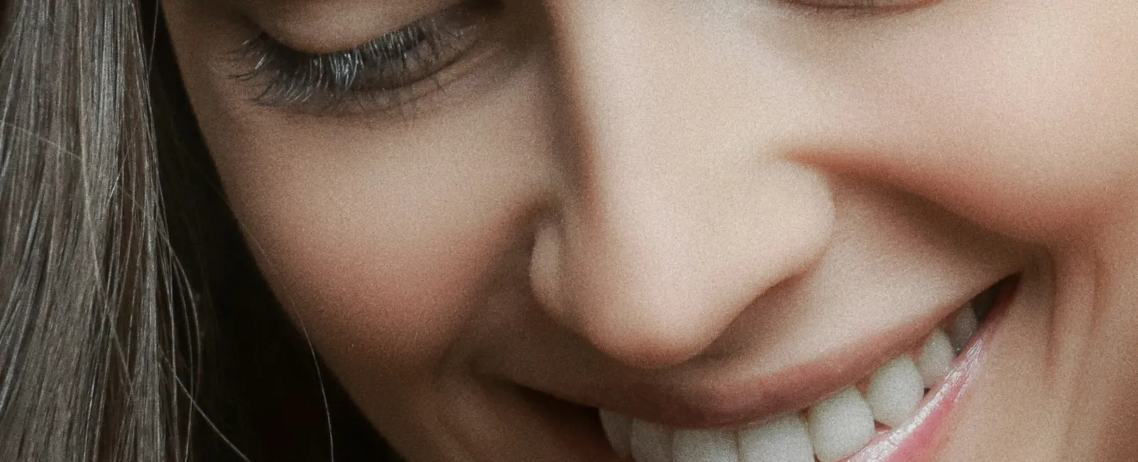 Close-up of a smiling woman with long dark hair and clear skin looking downwards.