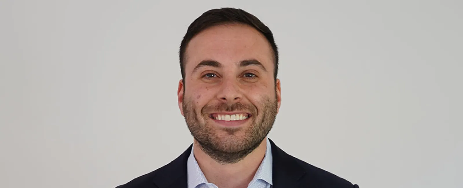 Professional man in a suit smiling against a plain background, showcasing a confident demeanor.