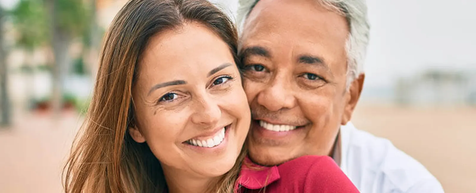 Happy couple embracing outdoors, smiling at the camera, showcasing love and connection in a scenic setting.