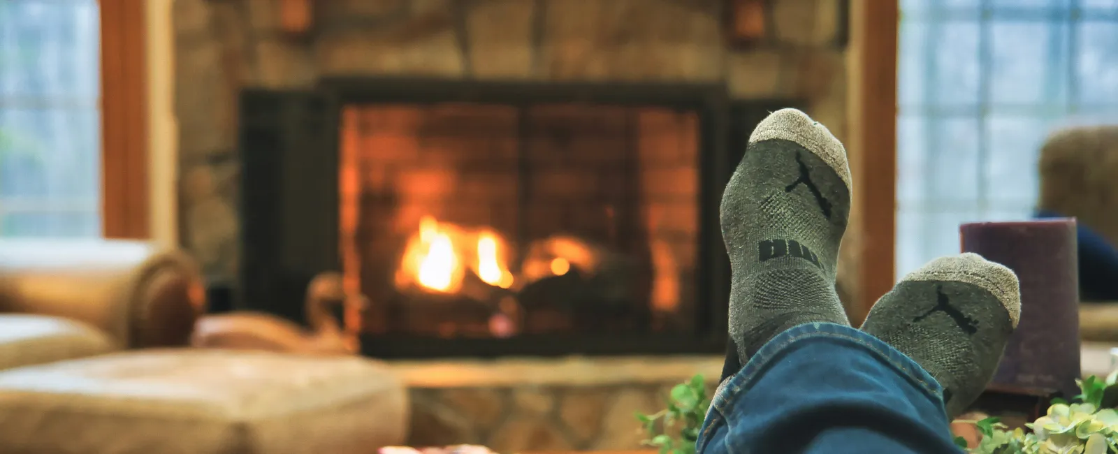 Person relaxing with feet up wearing socks near a cozy fireplace in a warm living room setting.