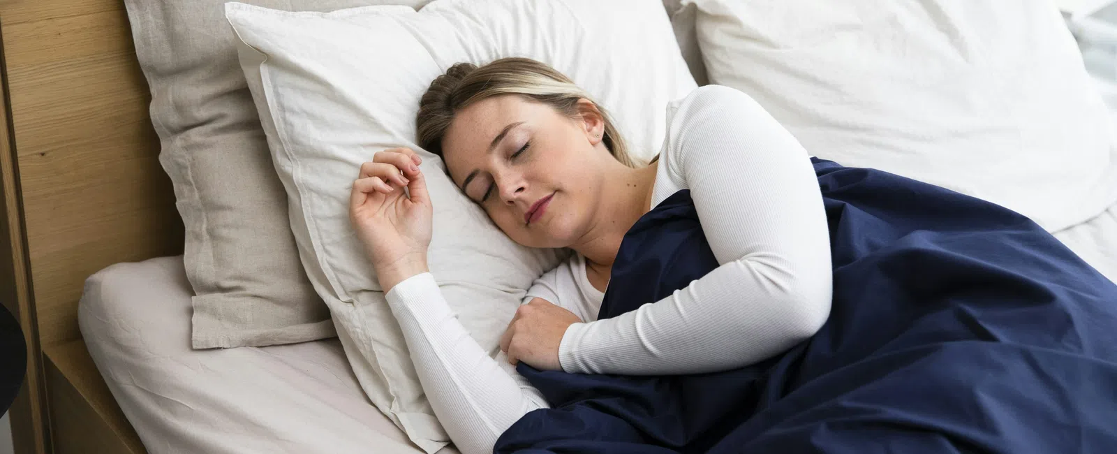 Woman peacefully sleeping on bed with white pillows and navy blue blanket in cozy bedroom.