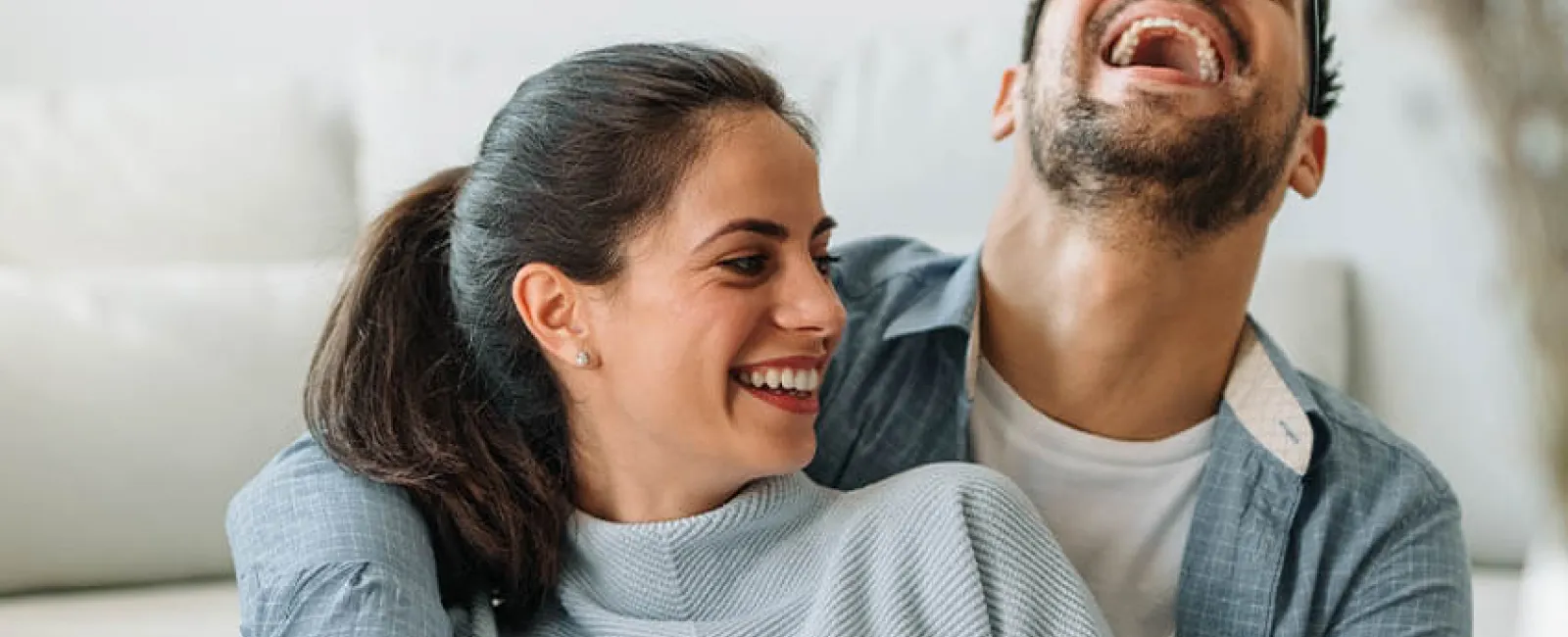 Happy couple laughing together on a couch in a bright and cozy living room.