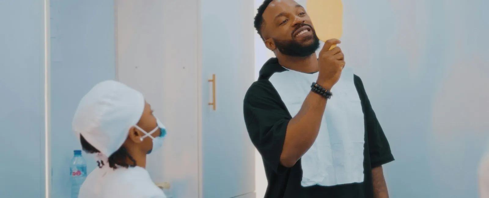 Man smiling while looking at a dental mirror held by a dentist in a clinic setting