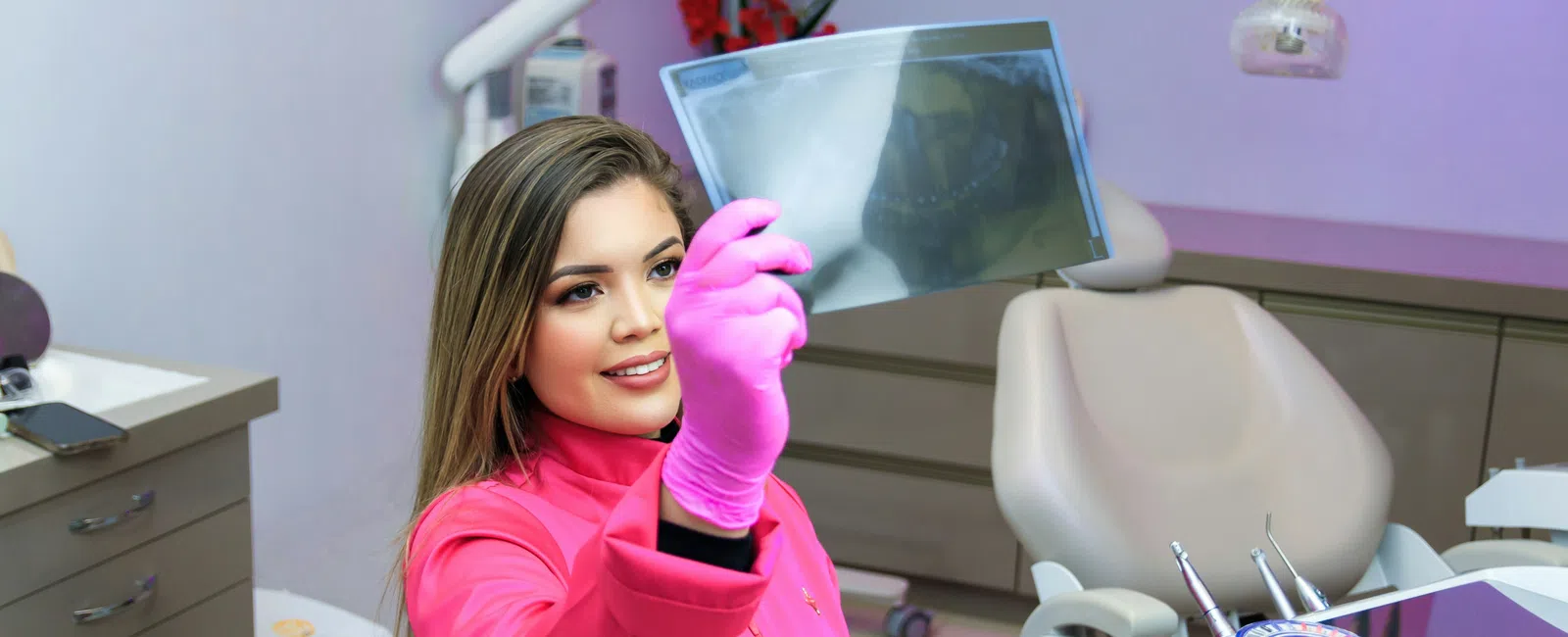 Female dentist in pink gloves examining dental X-ray in a modern dental clinic with equipment