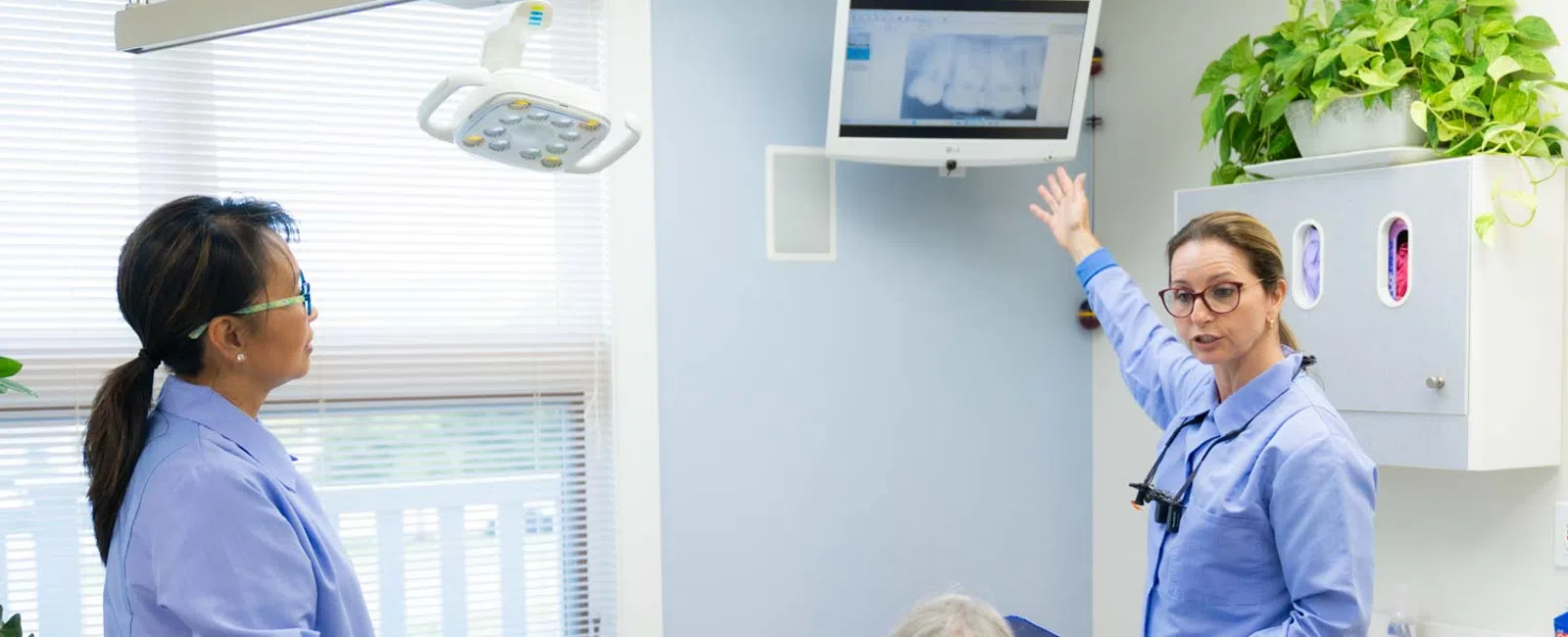 Dentist explaining dental X-ray results to a patient while another staff member observes in a bright clinic