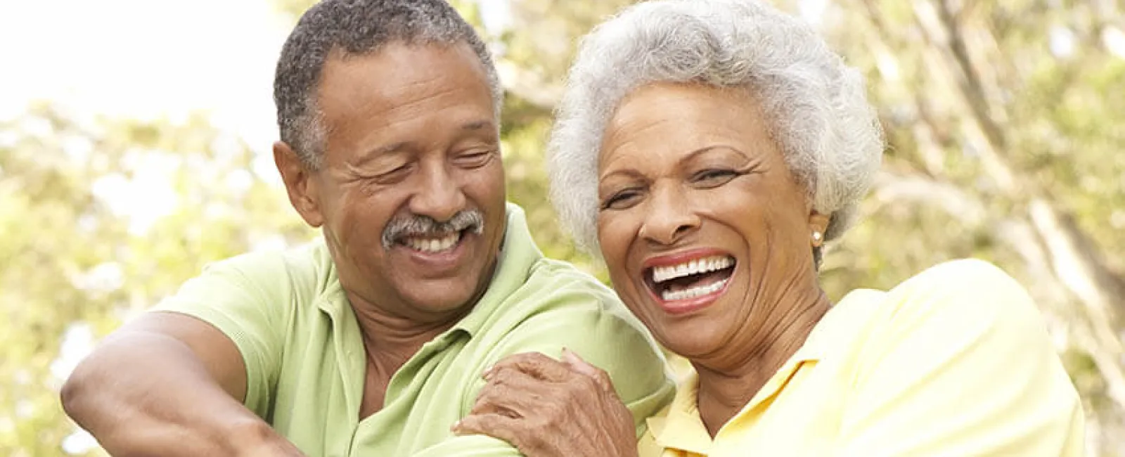 Happy older couple sitting outdoors laughing and enjoying a sunny day in casual clothes with rollerblades.
