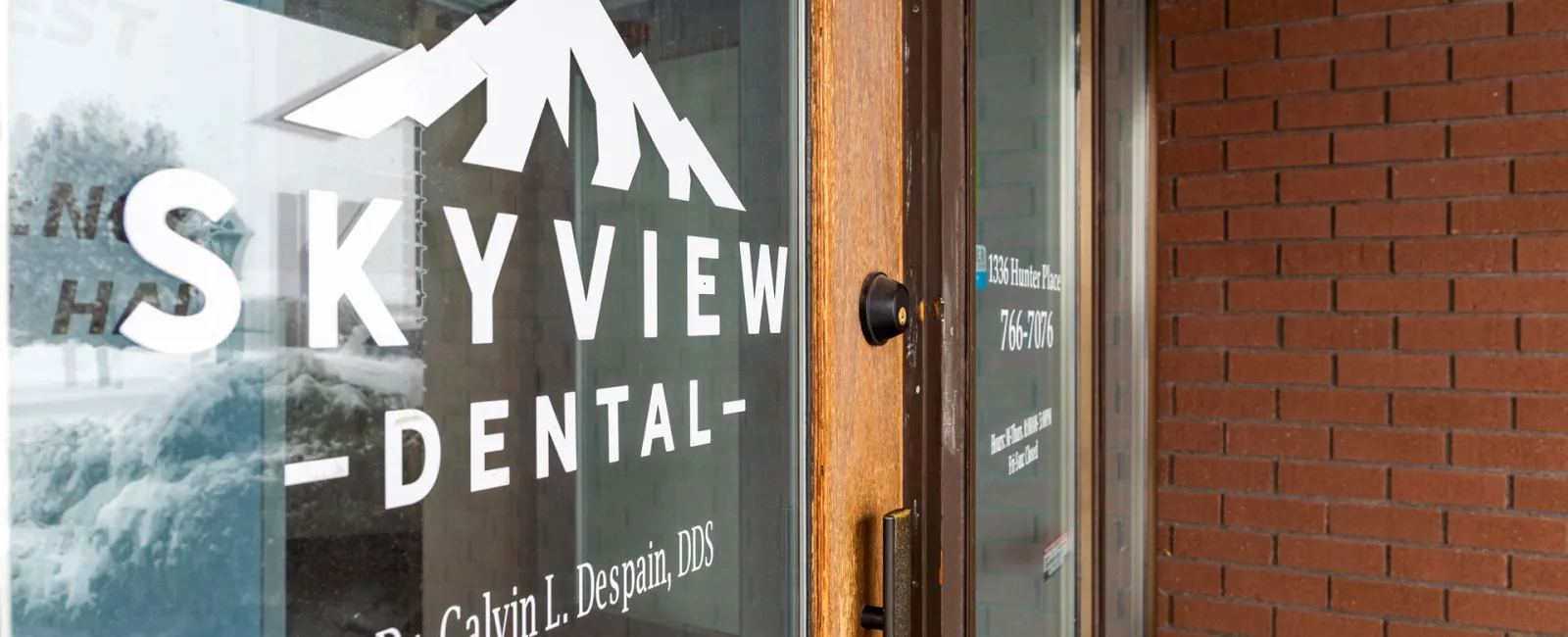 Glass door of Skyview Dental with white logo and Dr. Calvin L. Despain's name on a brick wall background.
