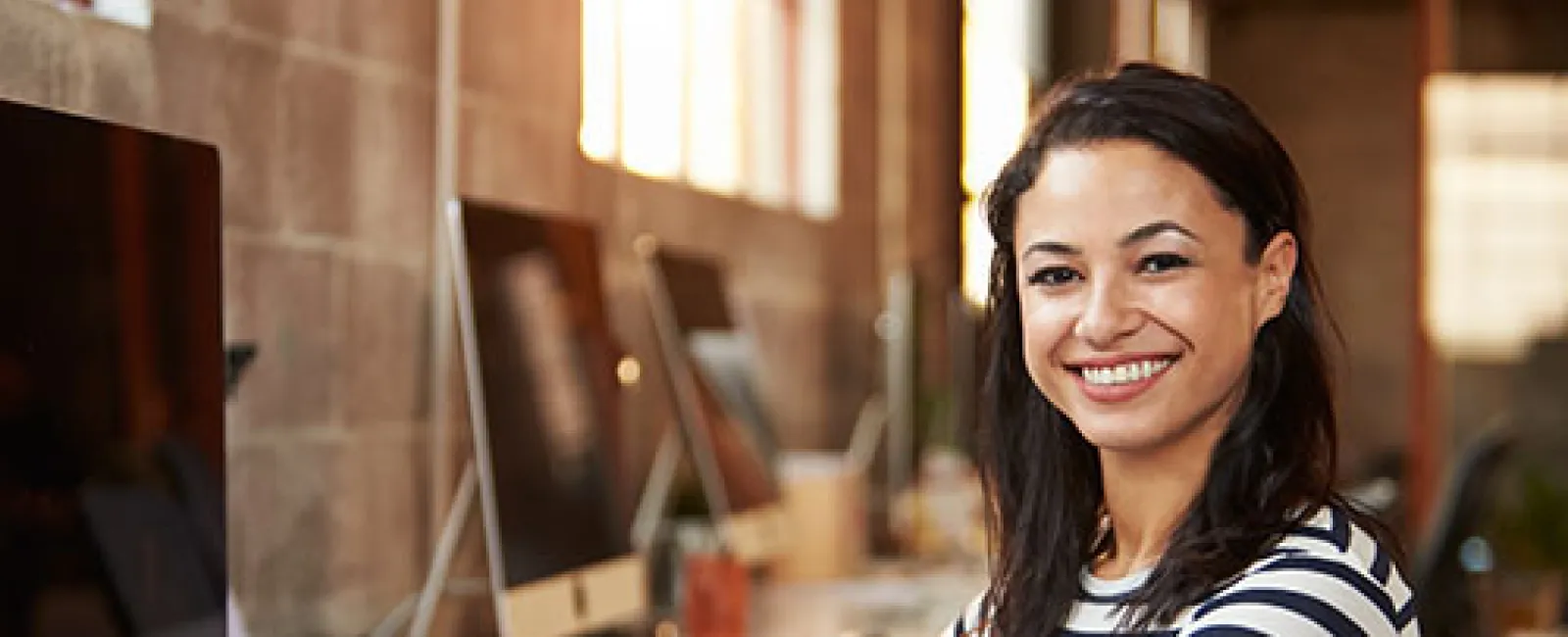 Smiling woman in striped shirt working on computer in modern bright office space