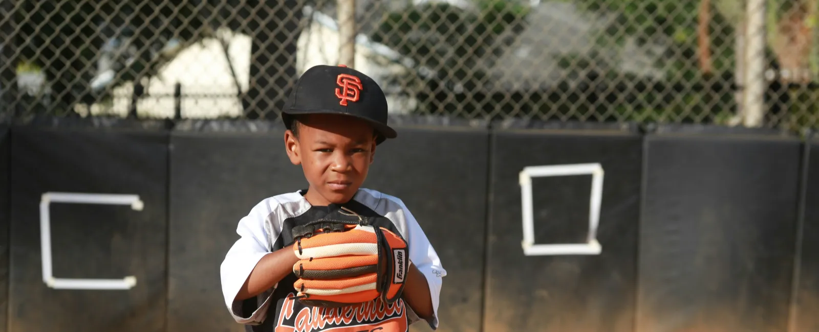 Young baseball player in Giants uniform standing on field ready to catch with glove.