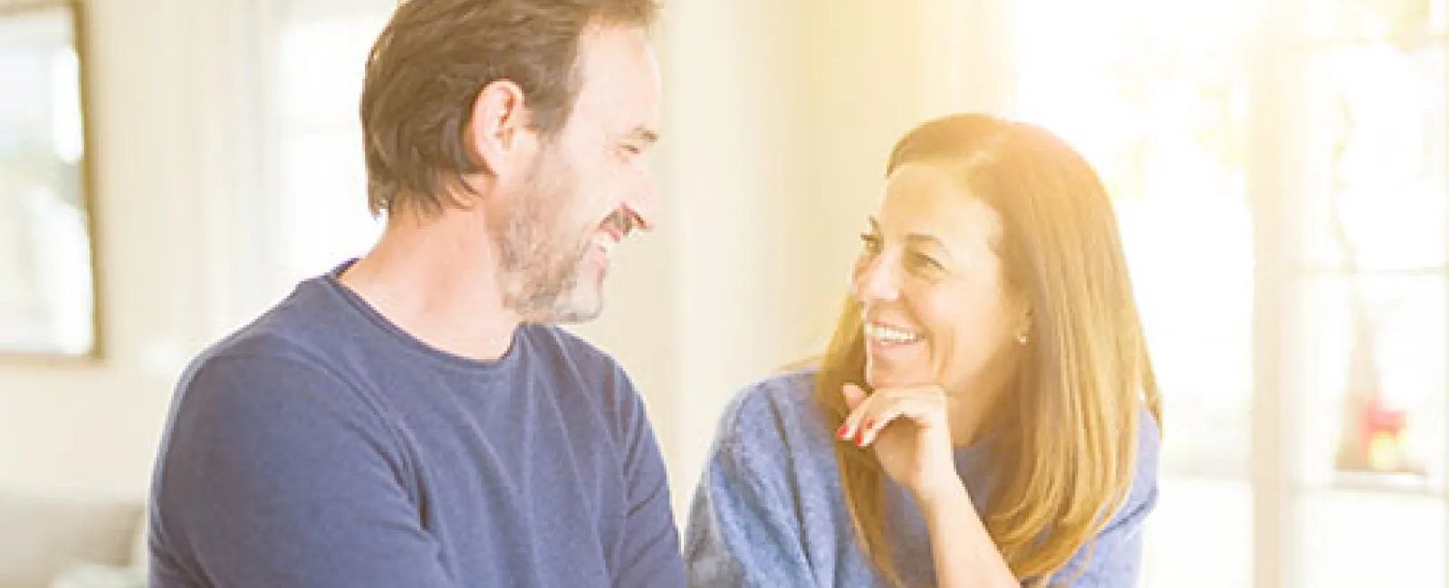 Middle-aged couple smiling and holding hands while sitting at a kitchen counter in bright sunlight