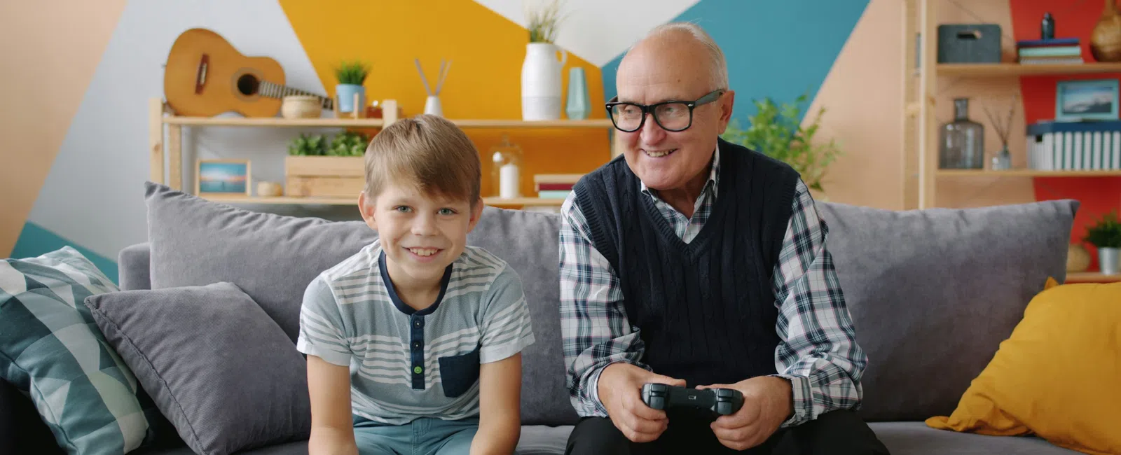 Grandfather and grandson happily playing video games together in a colorful living room setting.
