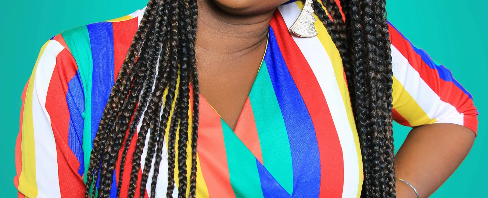 Smiling woman with long braids wearing a colorful striped dress against a teal background