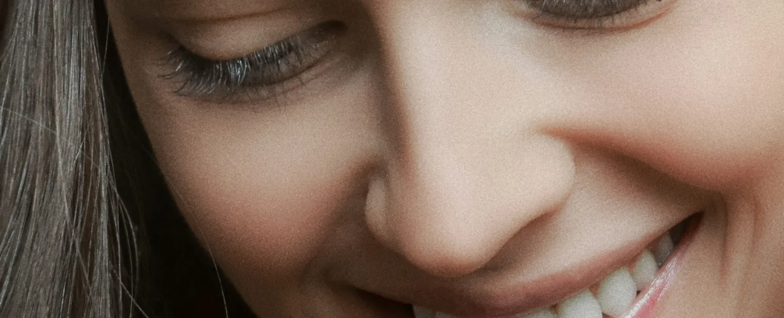 Close-up of a smiling woman with long hair and clear skin looking down, showing natural beauty