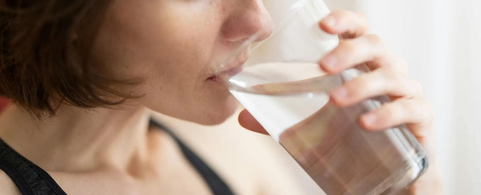 Close-up of a woman drinking clear water from a transparent glass indoors in soft natural light.