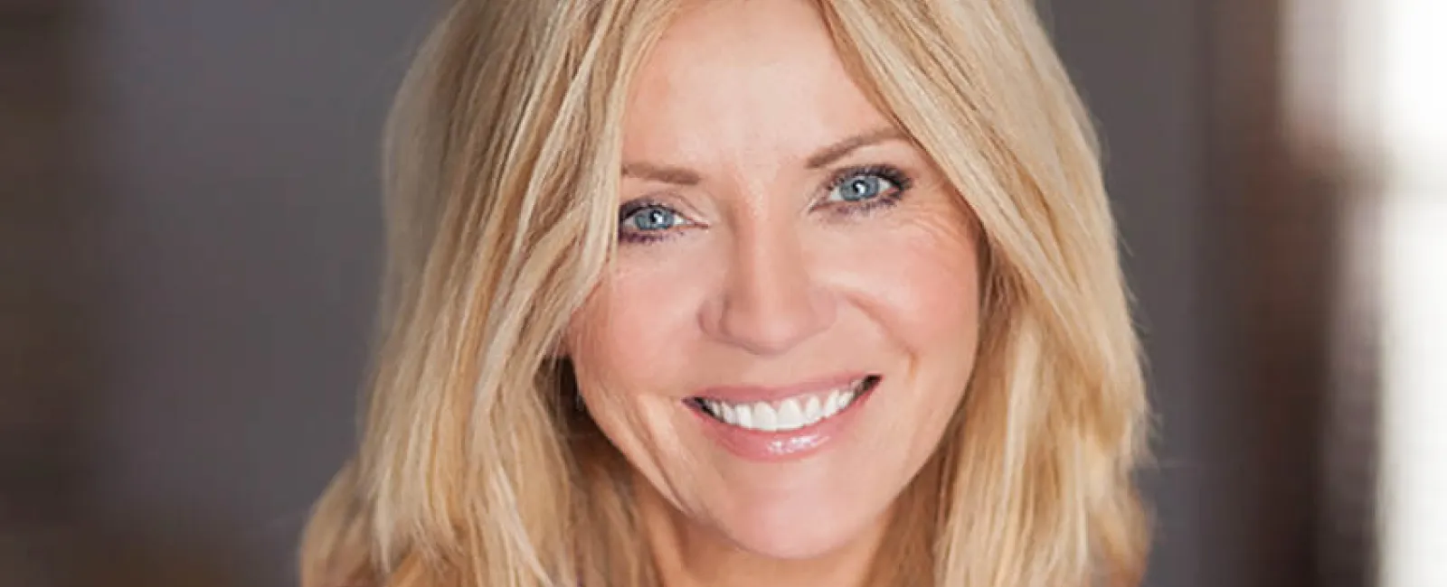 Smiling woman with blonde hair wearing a purple blouse, showcasing a warm and friendly demeanor.