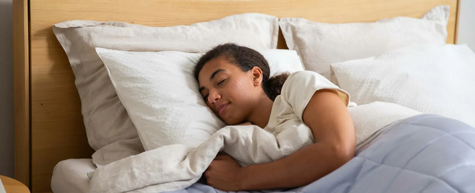 Woman sleeping peacefully in bed with white pillows and light blue comforter under soft natural light.